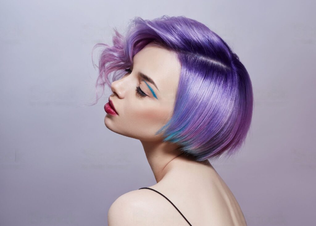 Portrait of a woman with bright colored flying hair, all shades of purple. Hair coloring, beautiful lips and makeup. Hair fluttering in the wind. Sexy girl with short hair.
